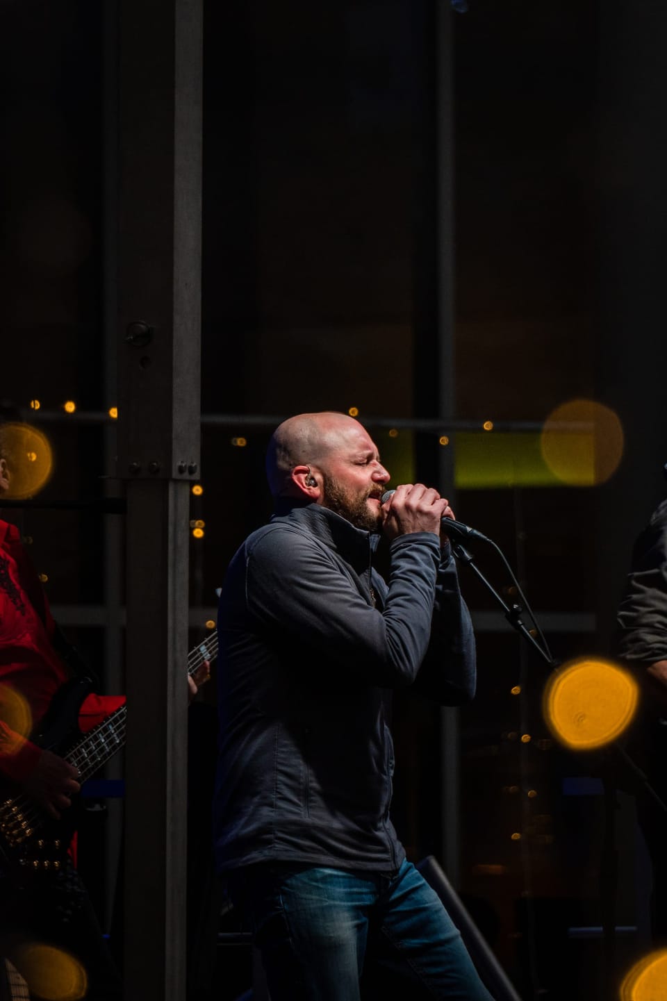 Bearded singer performing into a microphone with warm bokeh lights