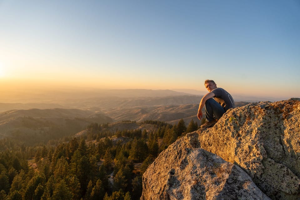 Man sitting on a granite boulder watching the sunset over hazy forested mountains