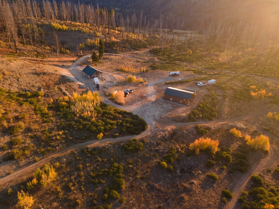 Aerial drone view of cabins, dirt roads, and trees glowing in golden-hour light