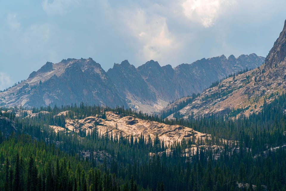 Jagged mountain peaks above forested valleys with scattered clouds
