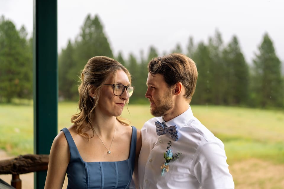 Couple in a blue dress and bow tie smiling at each other on a porch overlooking green fields