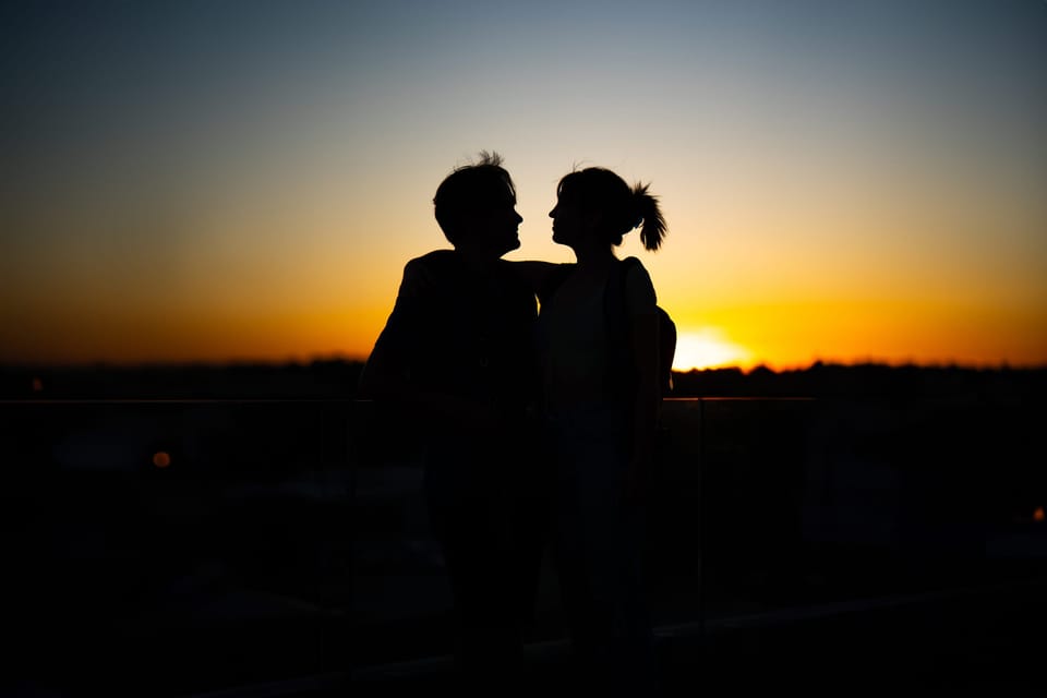 Couple silhouetted face to face against an orange sunset horizon