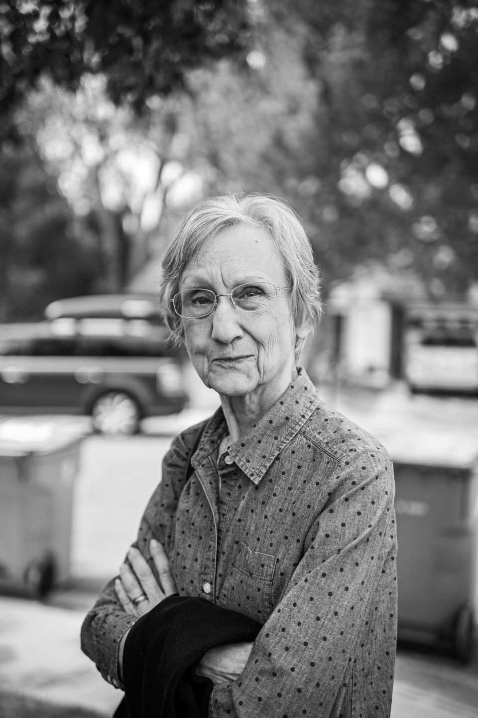 Black-and-white portrait of an older woman with arms crossed, standing outdoors
