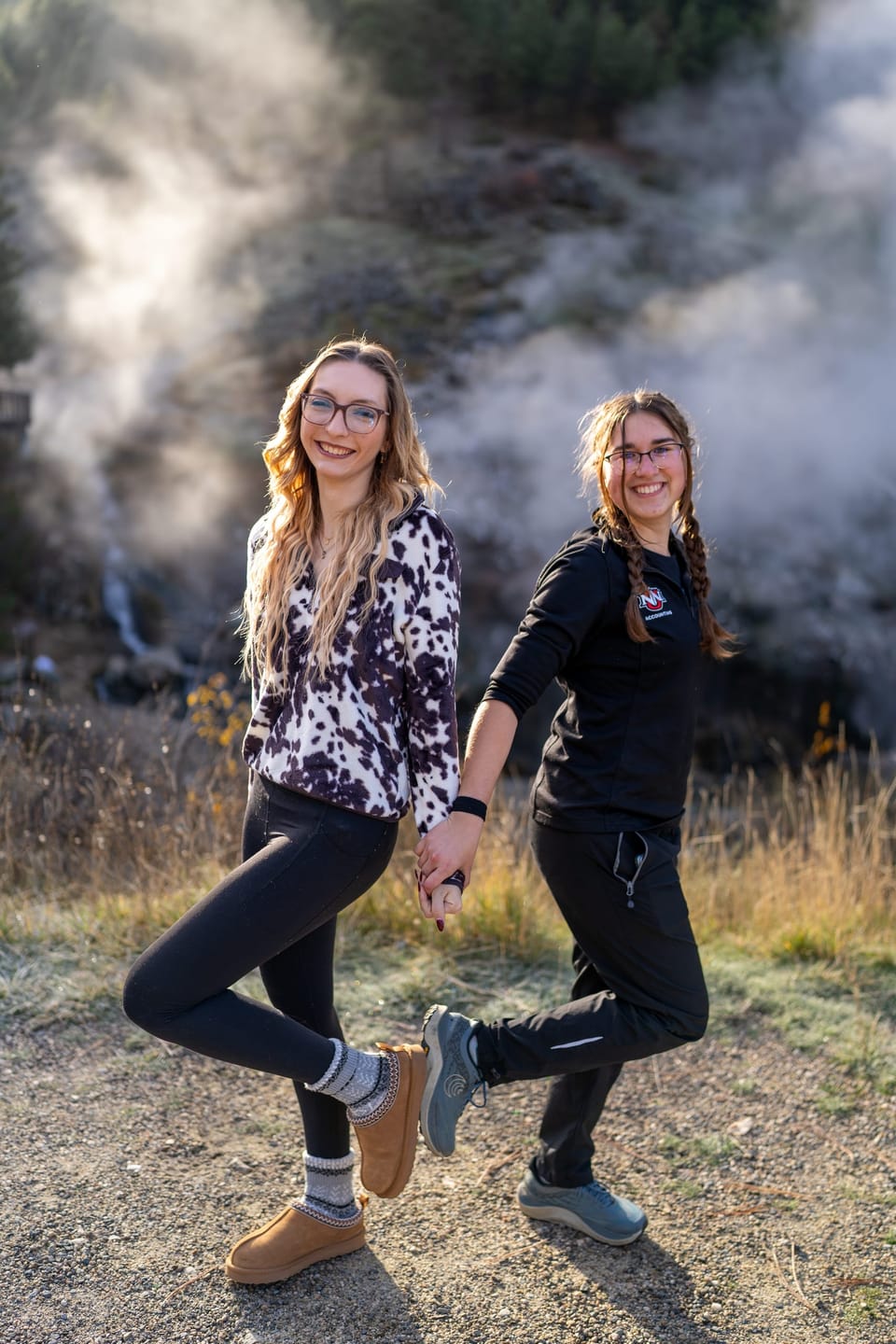 Two women posing playfully beside steaming geothermal vents