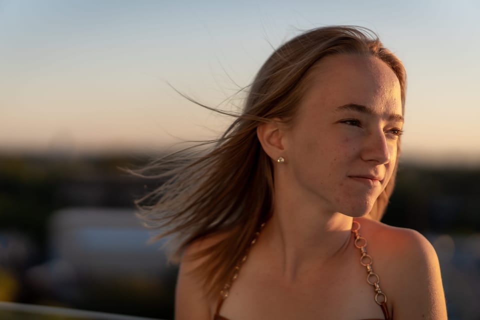 Young woman with windblown hair in warm golden-hour backlight, city blurred behind her
