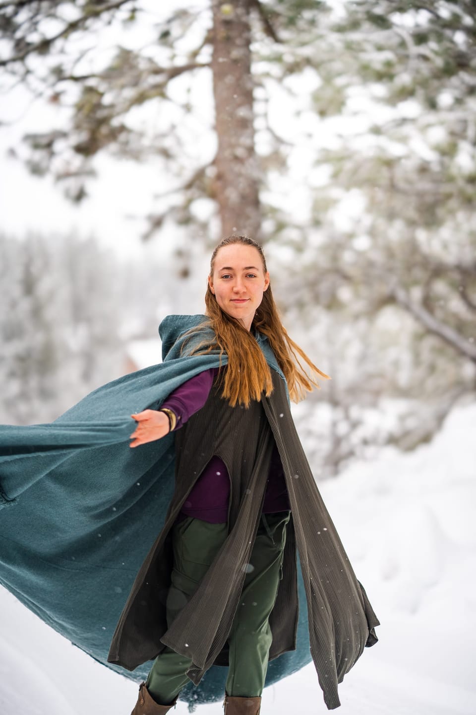 Woman in a flowing green cloak twirling in a snowy forest