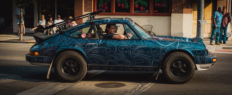 Vintage Porsche with a teal topographic-pattern wrap and roof rack driving downtown