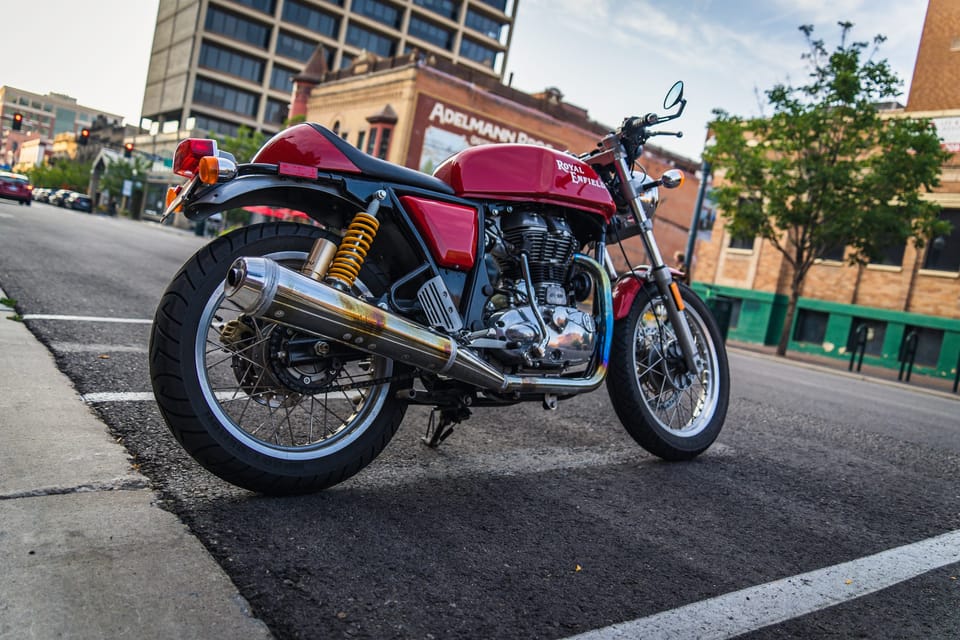 Red cafe-racer motorcycle parked at a downtown curb beside historic brick buildings