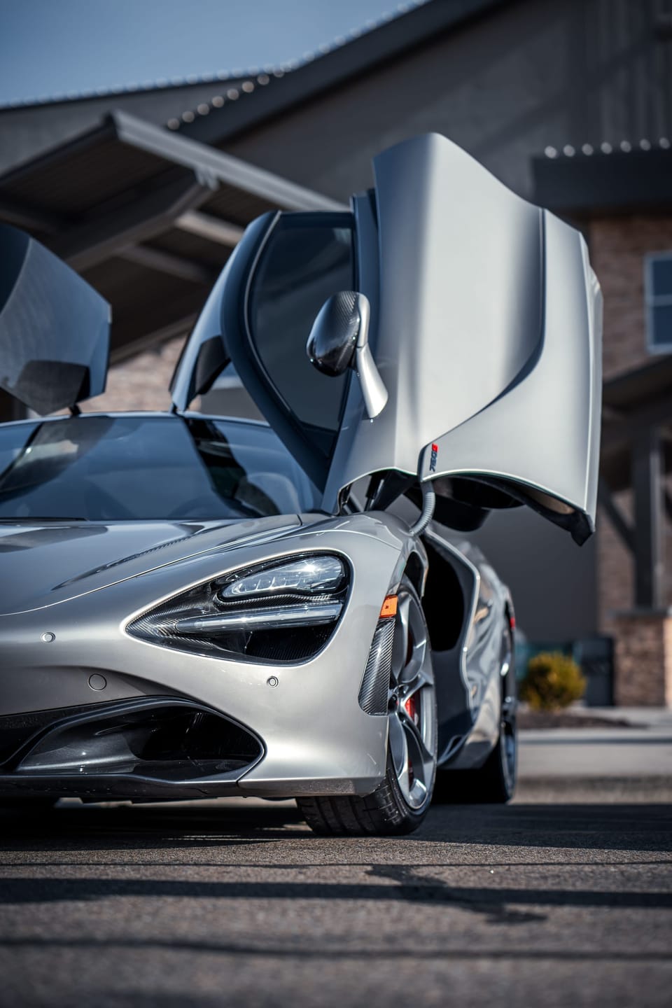 Silver McLaren supercar with both dihedral doors raised, shot from a low angle