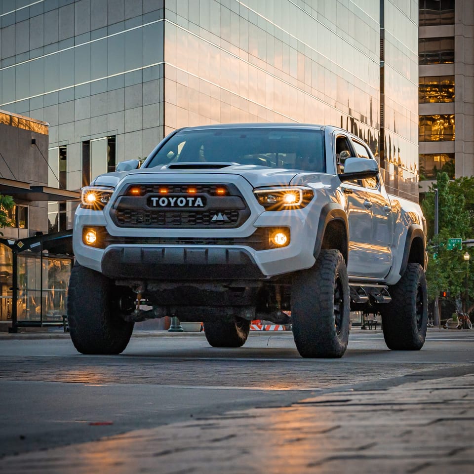 Gray lifted Toyota Tacoma in front of downtown glass buildings at golden hour