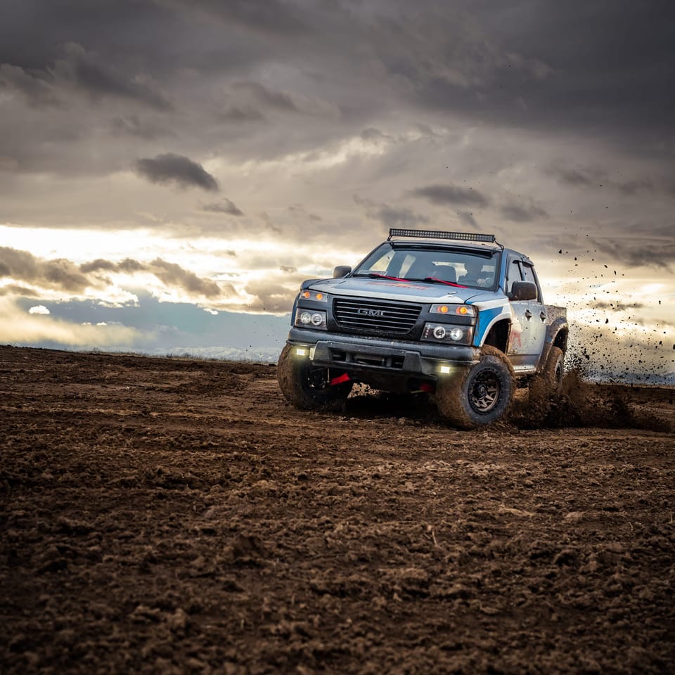 Gray off-road pickup throwing dirt as it drives across a plowed field under dramatic clouds