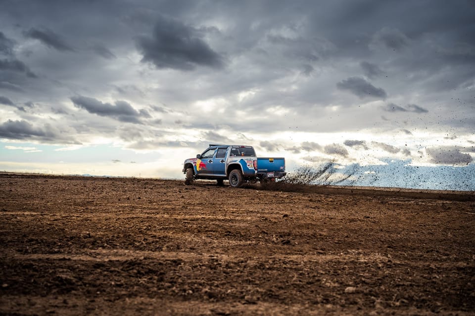 Pickup truck on a rise in a plowed dirt field beneath a stormy, cloudy sky