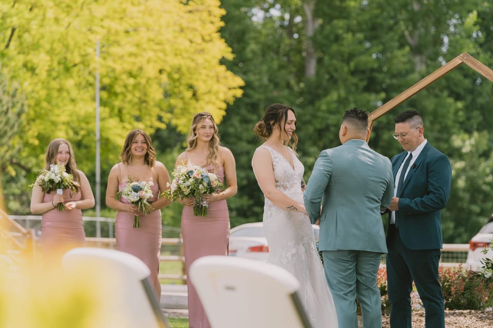 Bridesmaids in dusty rose dresses watching the bride and groom at an outdoor ceremony