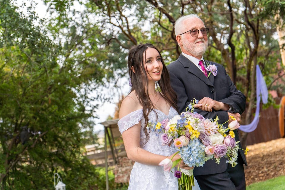 Bride with a pastel bouquet walking arm in arm with her father