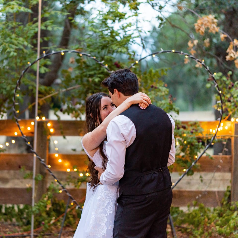 Bride and groom embracing in front of a heart-shaped arch strung with lights