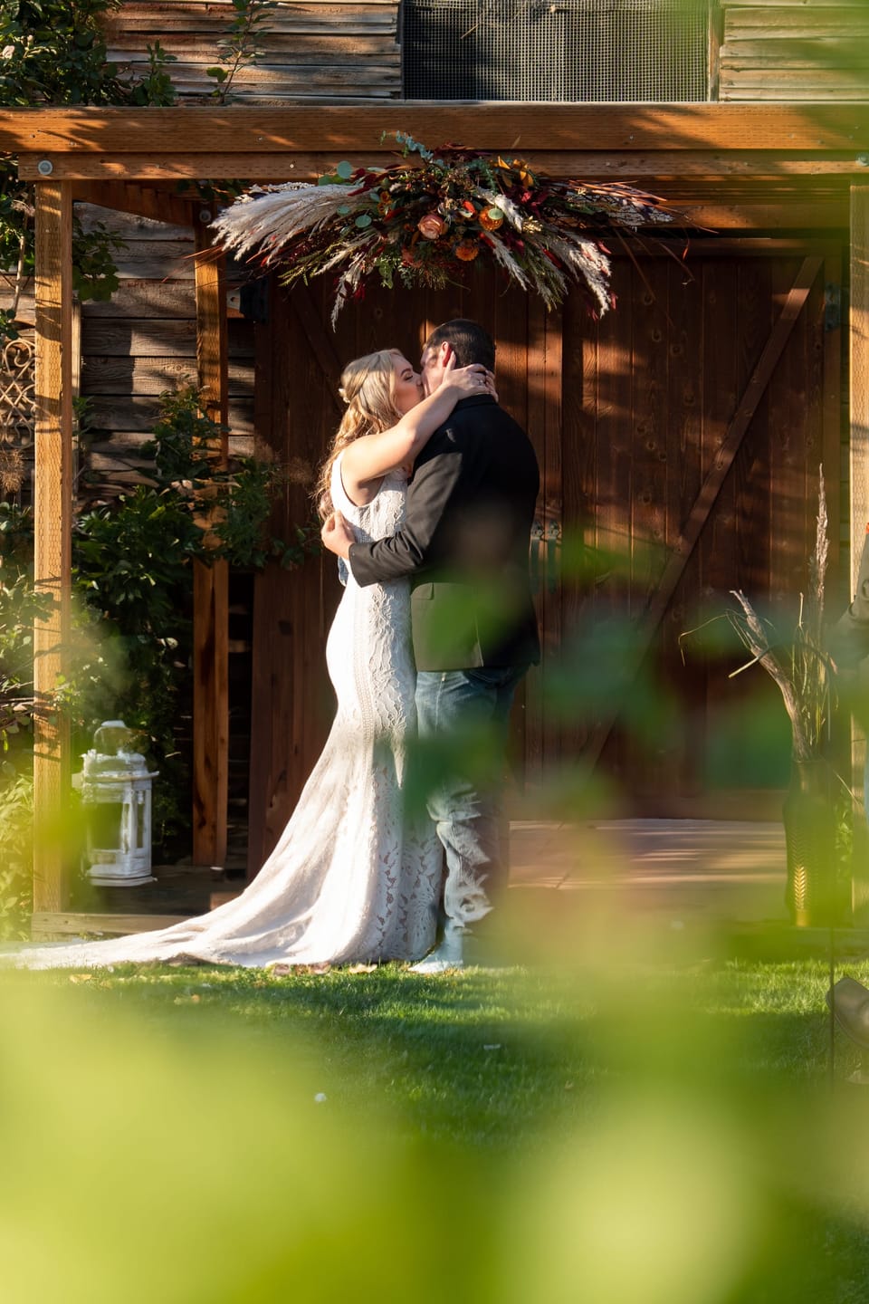 Bride and groom kissing under a wooden altar, framed by out-of-focus foliage
