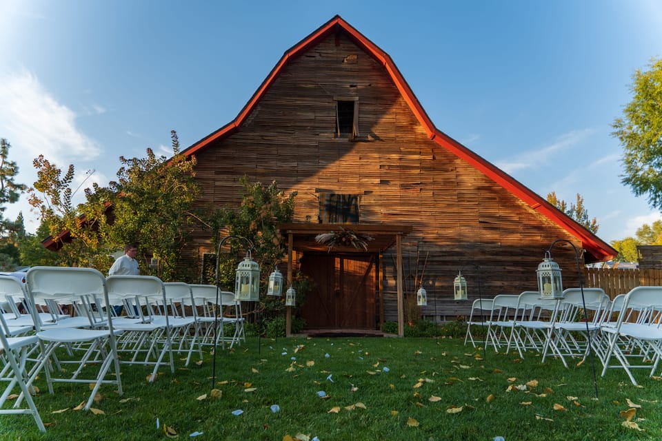 Red-roofed wooden barn with rows of white chairs on a lawn scattered with leaves