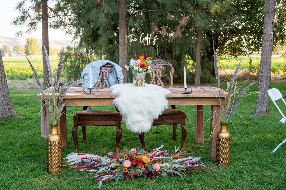 Outdoor sweetheart table with a white fur runner, gold vases, and floral arrangements
